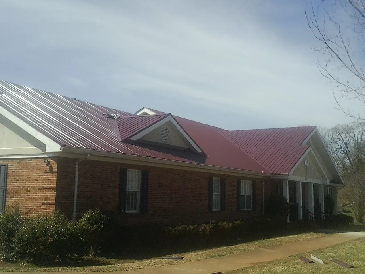 Red metal roof with gabled entries on a long brick building, from a Hail Damage Roof Repair job in Old Orchard Beach