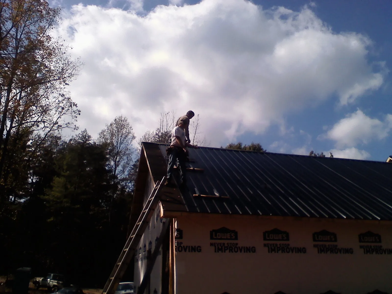 Roofer fastening dark metal panels high against a cloudy sky, from a Roof Inspection job in Old Orchard Beach