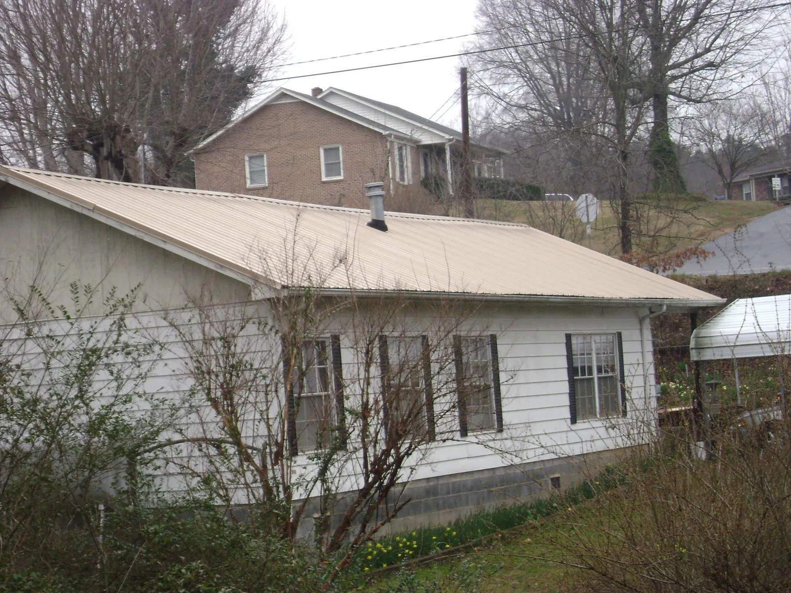 Tan metal roof on a white sided house set into a hillside — Commercial Roofing by Roofing Brothers in Old Orchard Beach